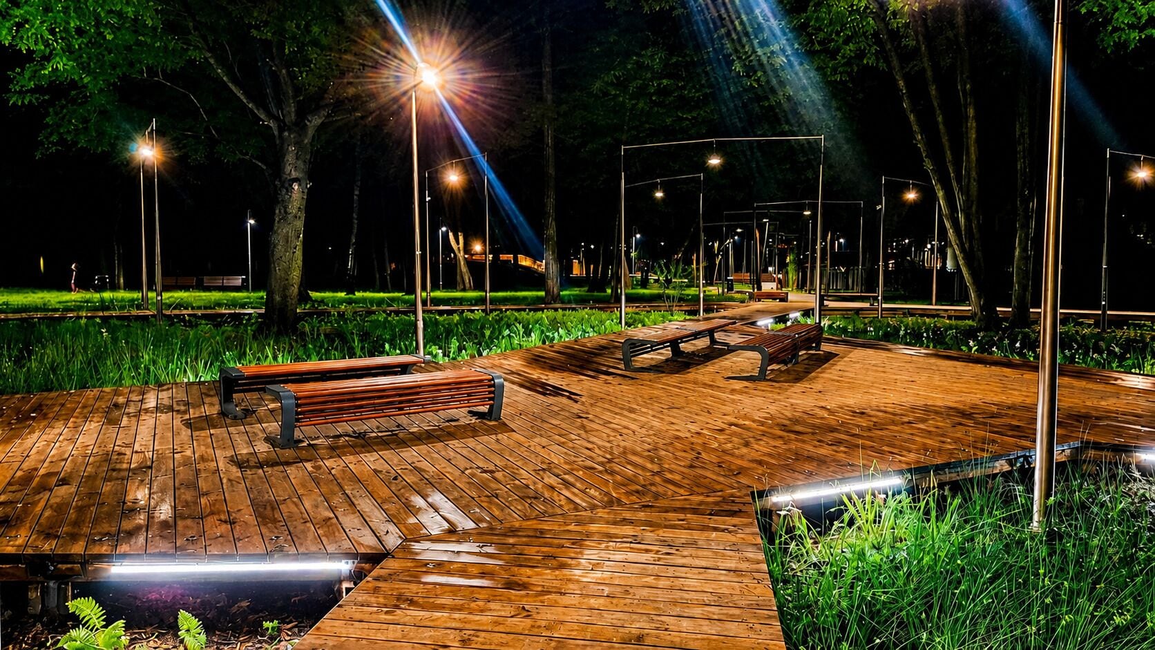 Un parc nocturne doté de sentiers en bois, de bancs et de lampadaires.