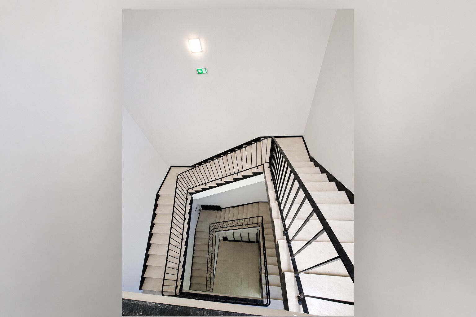 Un escalier moderne au design géométrique, doté d’une rampe et d’un luminaire fixé au plafond.