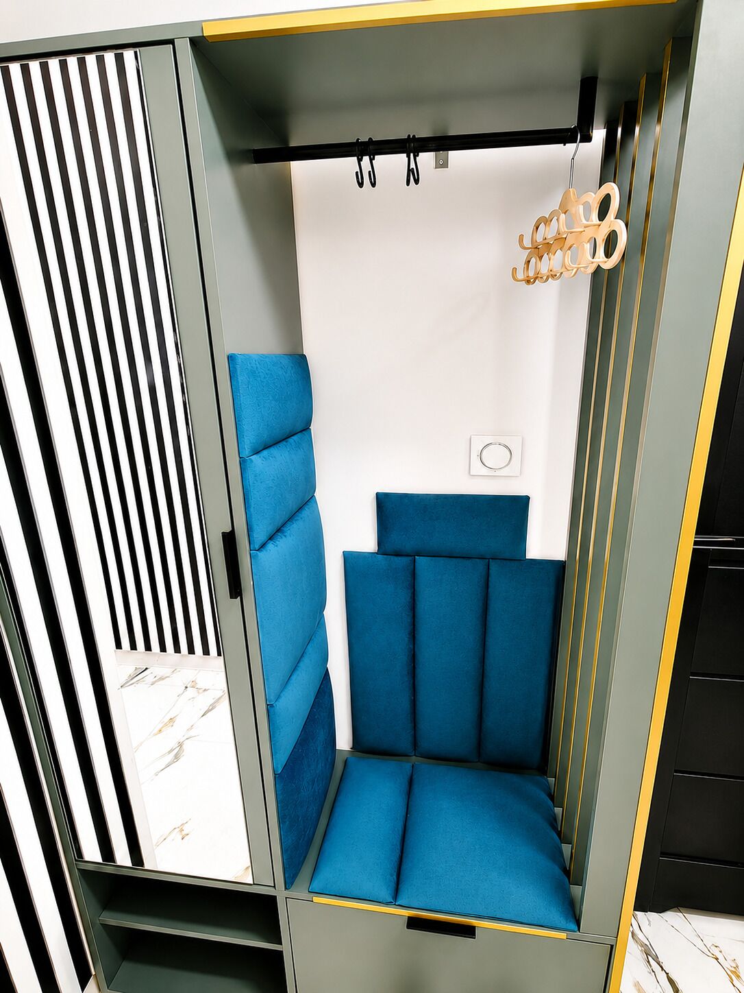 Une pièce dotée d’un coin salon avec des sièges recouverts d’un tissu bleu, d’un panneau à rayures verticales et d’un luminaire suspendu.