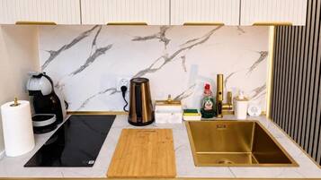 Una cocina moderna con salpicadero de mármol, placa de inducción negra, tabla de cortar de madera, pileta dorada y diversos electrodomésticos de cocina.