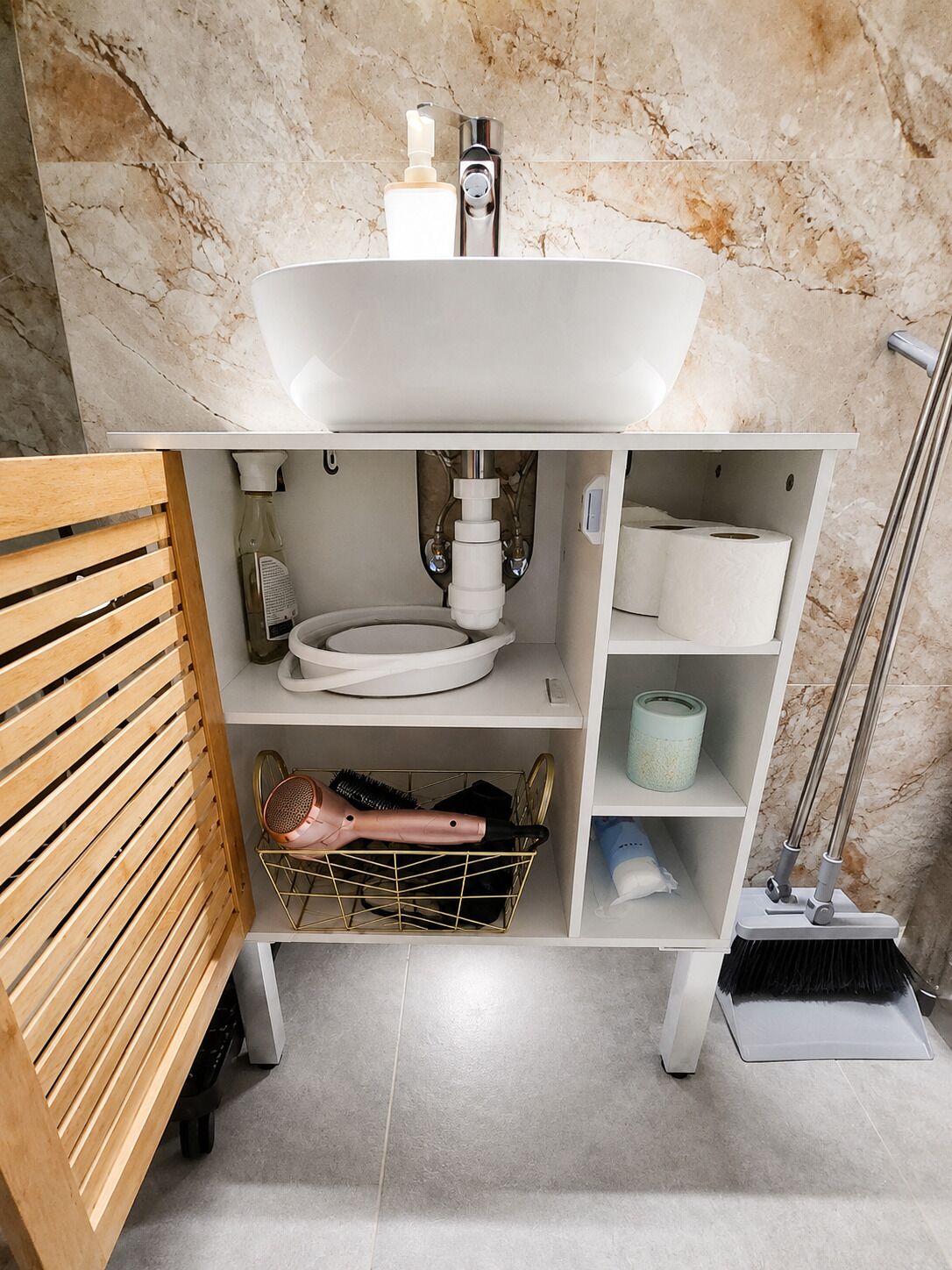 Un bagno con un lavandino bianco, carta igienica, un asciugacapelli e una scopa.