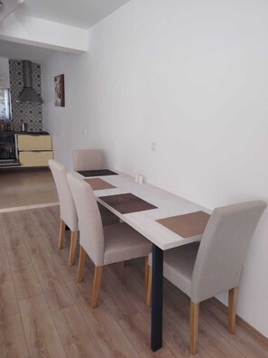 A dining area with a long table, four chairs, and a kitchen in the background. - Stunning 100m² Modern Townhouse with Sea Views & Private Garden (Ližnjan)