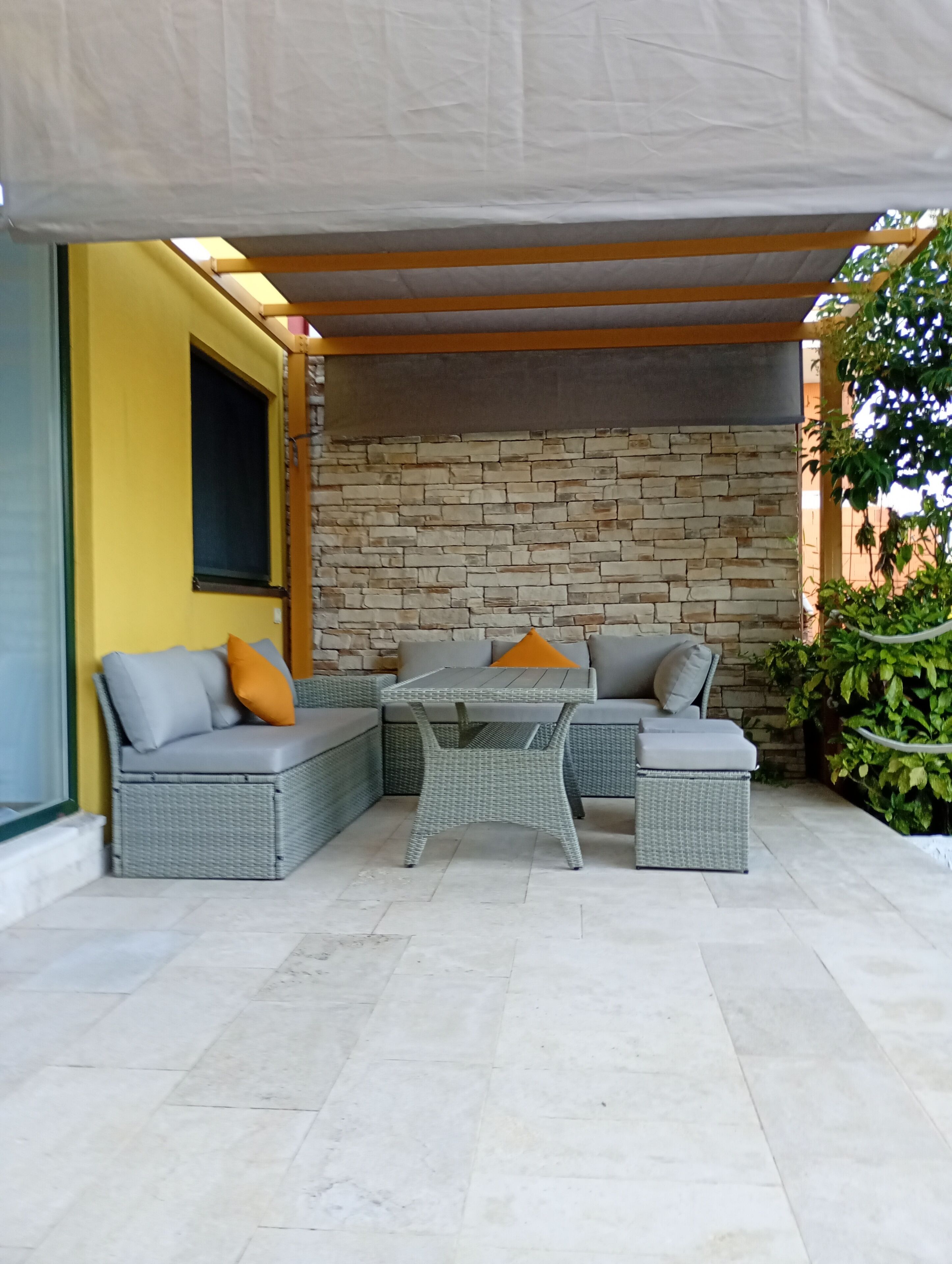 An outdoor seating area with a stone wall backdrop, a covered table, and cushioned seating.