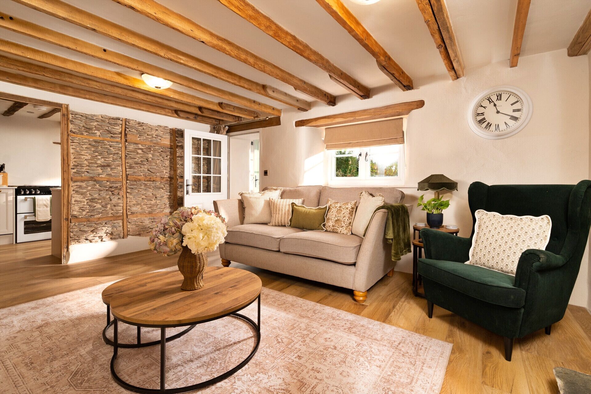 Un salon chaleureux avec un plafond en bois, un canapé, un fauteuil vert, une table basse ronde et une horloge au mur.