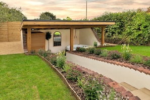 Un área de patio exterior moderna con un pergolado de madera, un jacuzzi y un jardín con diversas plantas y flores.