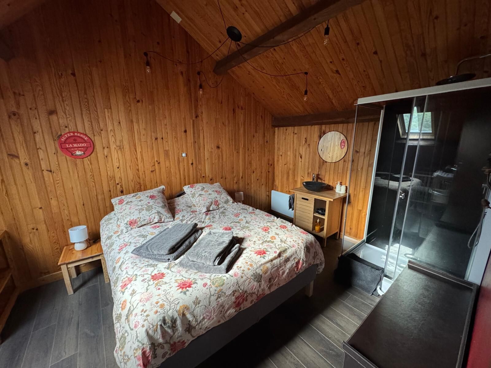 A wooden-paneled bedroom with a bed, bedside tables, a mirror, and a view of the outside.