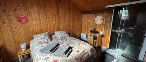 A wooden-paneled bedroom with a bed, bedside tables, a mirror, and a view of the outside.