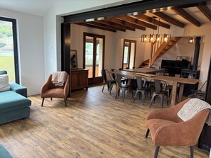 A spacious living area with a wooden floor, a sofa, a chair, and a dining table with chairs. There is a staircase leading to an upper level. - Chalet for rent with a south-facing heated outdoor pool   (Besse-et-Saint-Anastaise)
