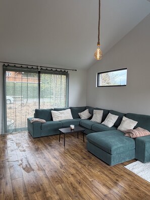 A modern living room with a sectional sofa, a coffee table, and a large window with a view of the outdoors. - Chalet for rent with a south-facing heated outdoor pool (Besse-et-Saint-Anastaise)