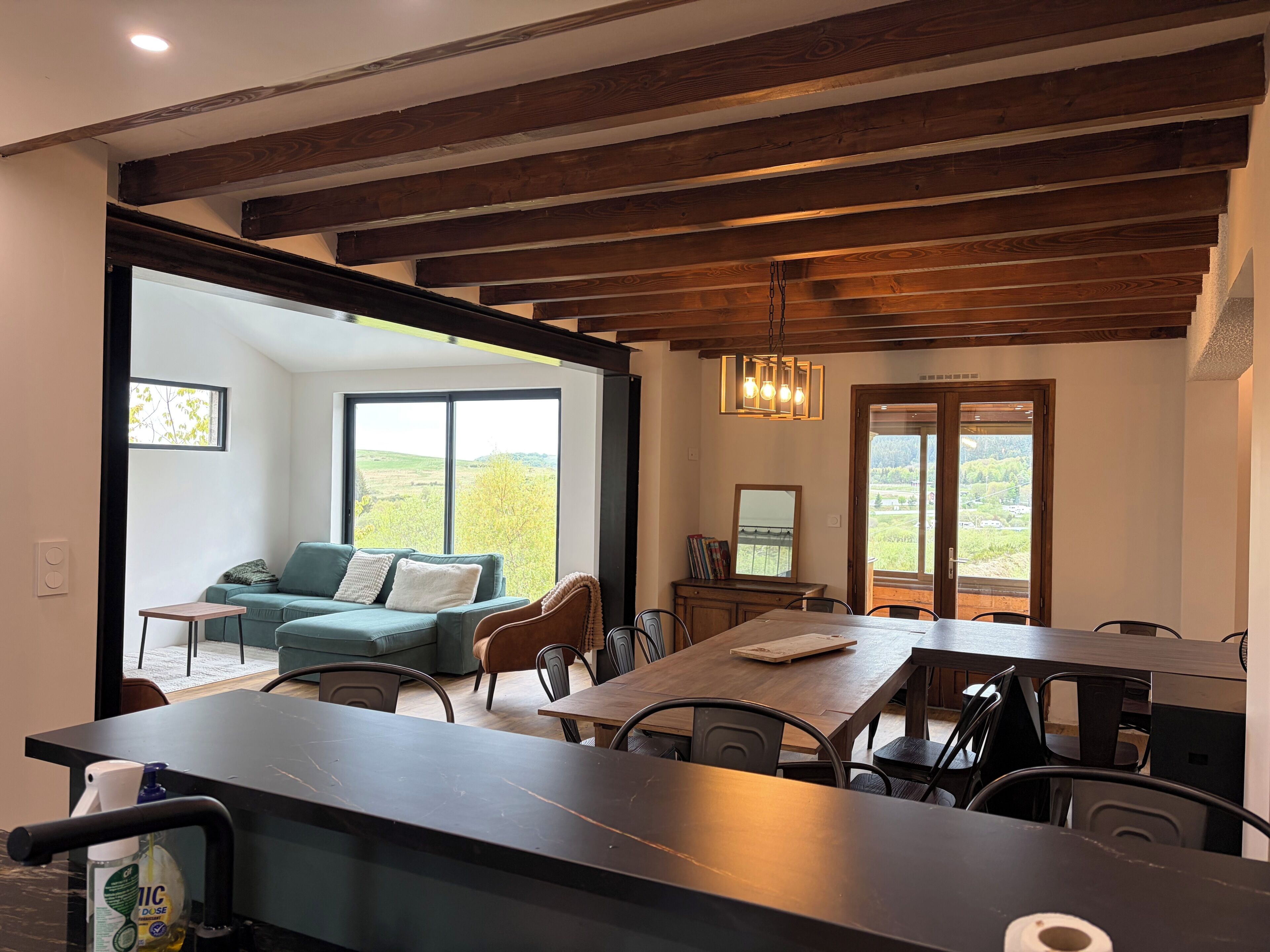 A modern dining area with a wooden ceiling, a large window offering a view of the outdoors, and a dining table with chairs.