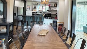 Een eetgedeelte met een houten tafel en metalen stoelen, een keuken op de achtergrond en een groot raam.