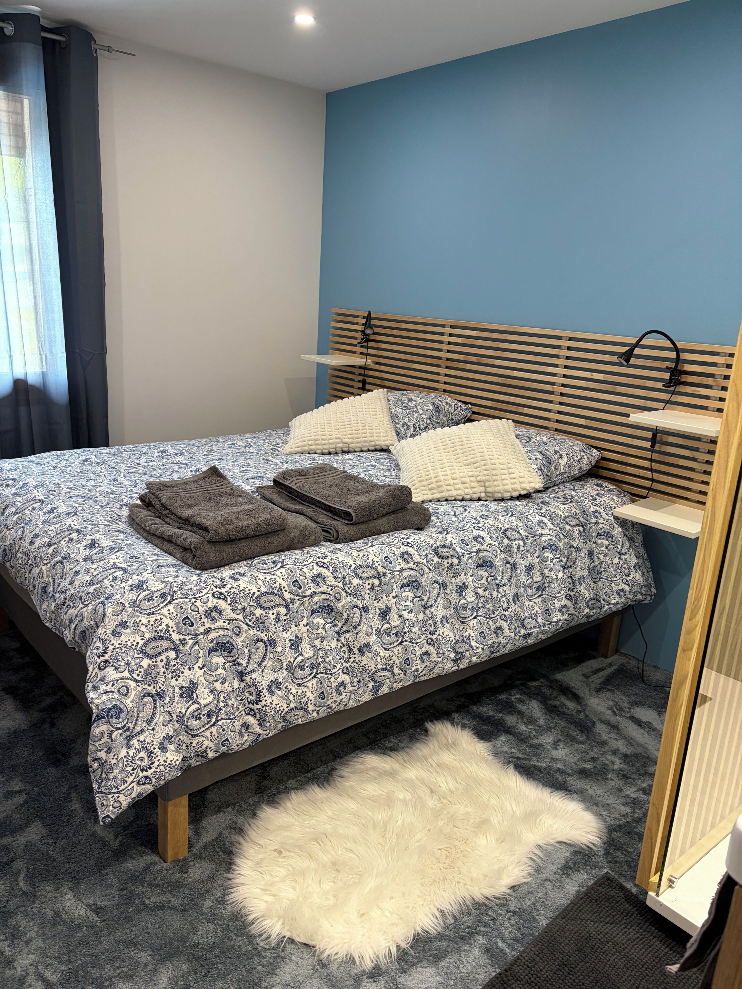 Une chambre à coucher avec un lit, des oreillers, un tapis moelleux, une table de chevet et une lampe.