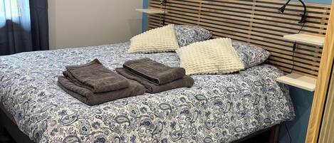 A bedroom with a bed, pillows, a fluffy rug, a bedside table, and a lamp.