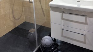 Een badkamer met een douche met glazen wanden, een wit wastafelmeubel met spiegel en een zwarte prullenbak.