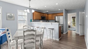 A modern kitchen with wooden cabinets, stainless steel appliances, and a central island with bar stools. - Coco Beach - Walk to Carolina Beach, Family Friendly Townhome (Carolina Beach)