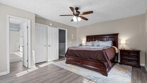 A bedroom with a bed, nightstands, a ceiling fan, and a walk-in closet. - Coco Beach - Walk to Carolina Beach, Family Friendly Townhome (Carolina Beach)