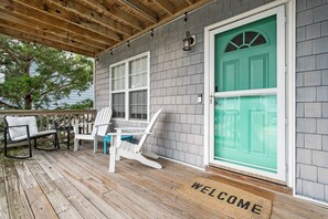 Eine überdachte Veranda mit Holzterrasse, einem weißen Stuhl, einem blauen Stuhl und einer grünen Tür mit Fußmatte.