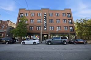 A multi-story building with a prominent 'BROOKLYN' sign, a storefront with a 'NORTH DOOR' sign, and several parked cars in front. - Brooklyn Arts Condo | Walk to Everything (Wilmington)