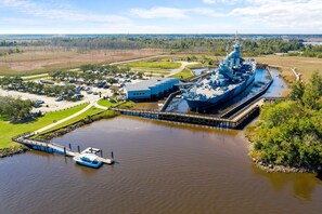 A large naval ship docked at a pier with a small boat moored nearby. - Brooklyn Arts Condo | Walk to Everything (Wilmington)
