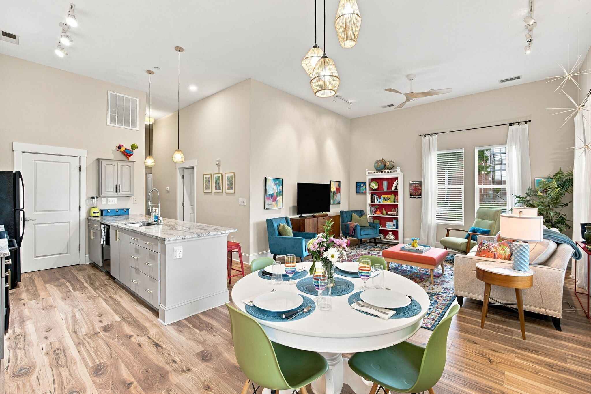 A modern kitchen with a central island, dining area with round table and chairs, and a living room with a sofa and chairs.