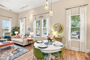 A modern living room with a sofa, coffee table, and dining area with a round table set for four. - Brooklyn Arts Condo | Walk to Everything (Wilmington)
