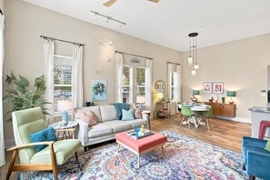 A living room with a sofa, coffee table, and chairs, a dining area with a table and chairs, and a kitchen area with a counter and appliances. - Brooklyn Arts Condo | Walk to Everything (Wilmington)