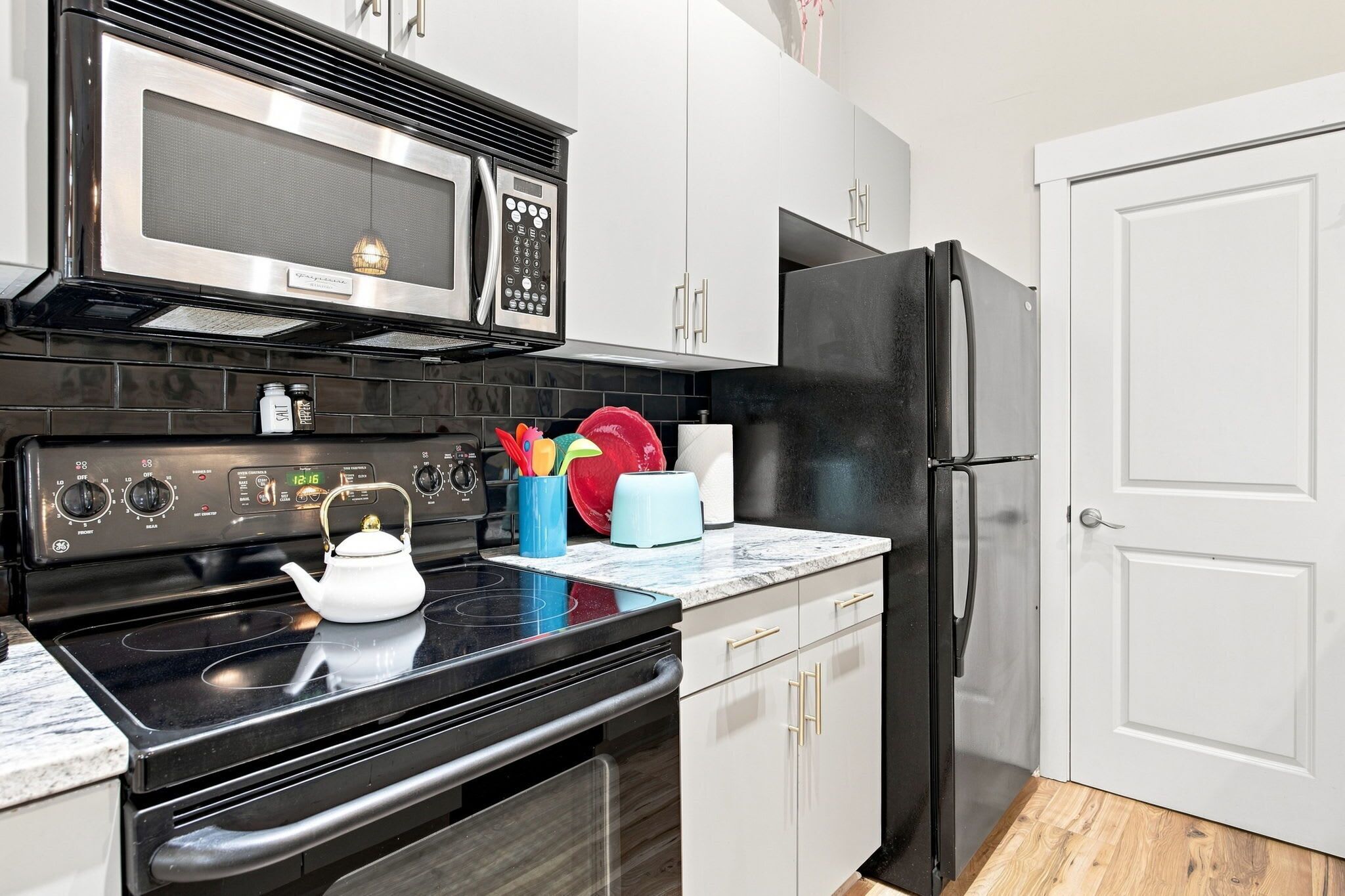 A kitchen with a black stove, a microwave, a refrigerator, and a tea kettle on the counter.