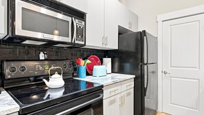Una cocina con estufa negra, microondas, refrigerador y hervidor sobre la encimera.