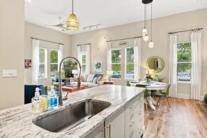 A modern kitchen with a marble countertop, a sink, and a dining area with a round table and chairs. - Brooklyn Arts Condo | Walk to Everything (Wilmington)
