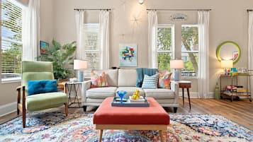 A living room with a sofa, armchairs, a coffee table, and a rug. There are windows with curtains, a wall clock, and a decorative star on the wall.