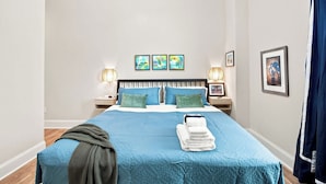 Una cama bien hecha con ropa de cama azul, dos lámparas de noche y una pila de toallas.