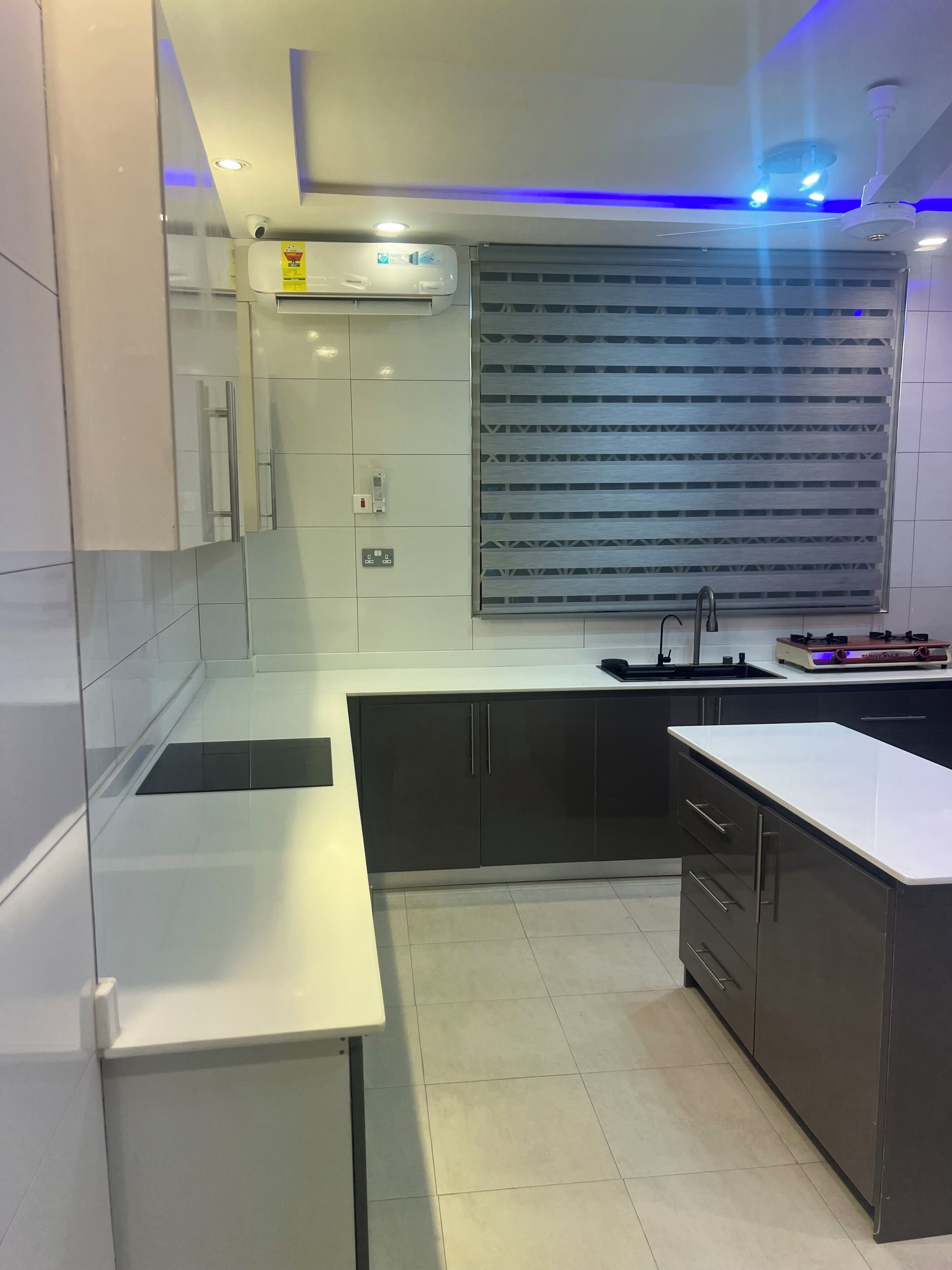 A modern kitchen with a built-in stove, a sink, and a window with blinds.