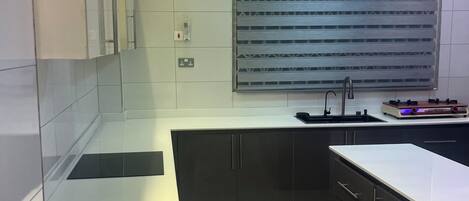 A modern kitchen with a built-in stove, a sink, and a window with blinds.