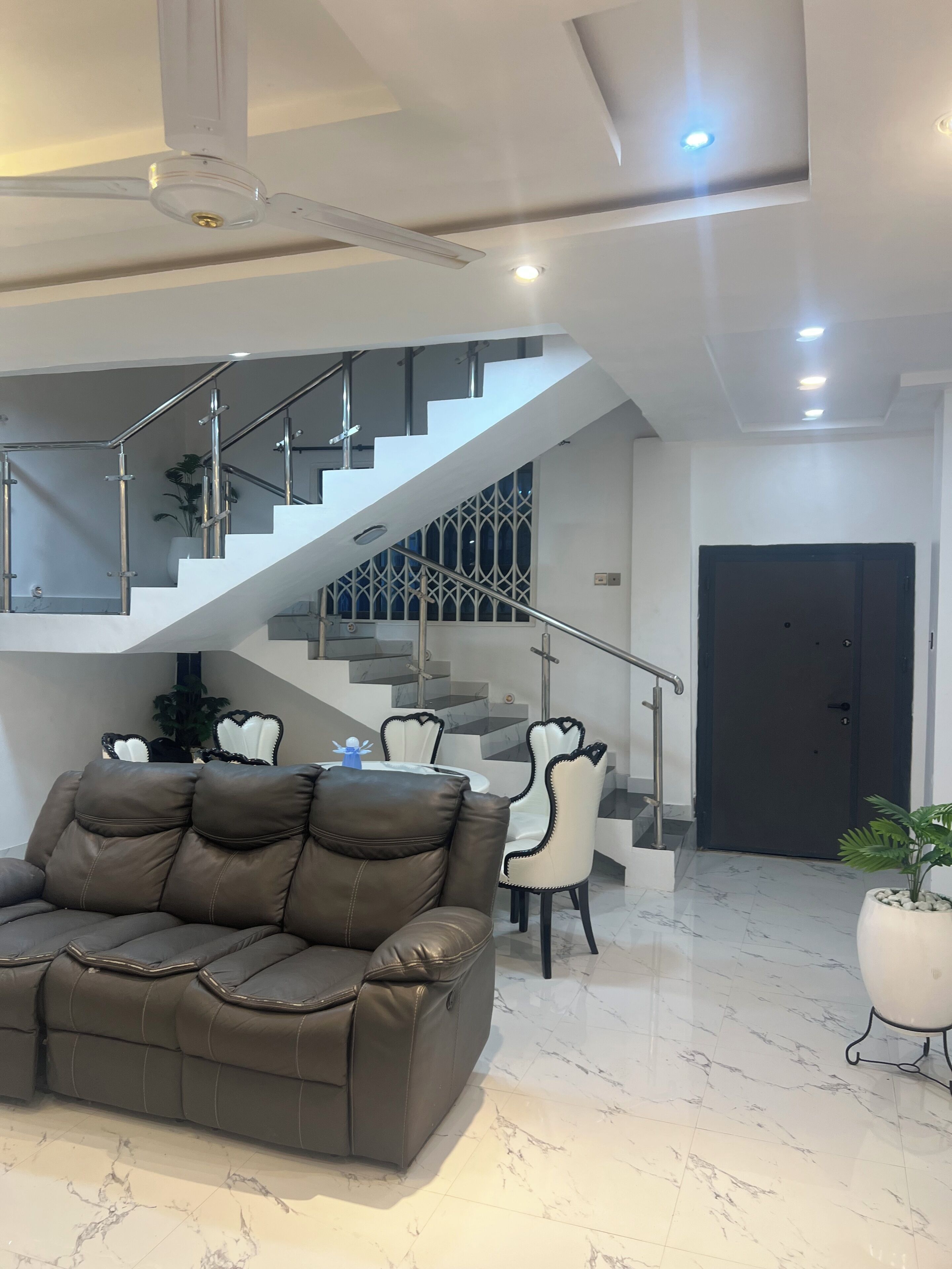 Una sala moderna con un sofá de cuero, un comedor con sillas, una escalera y una puerta.