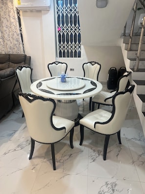 Een eetruimte met een ronde tafel en zes stoelen, een trap en een raam met een decoratief traliewerk.