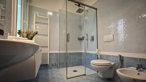 A bathroom with a glass-enclosed shower, a toilet, and two sinks. - Vrbo Property (Savigno)