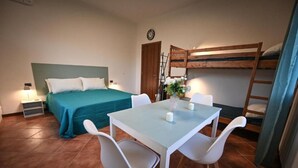 Een kamer met een bed, een tafel met stoelen, een stapelbed en een deur.
