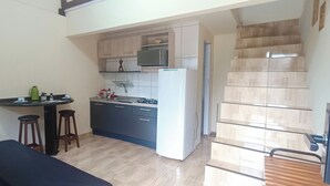 A compact kitchen with a gas stove, a microwave, and a refrigerator. There is a small dining area with stools. - Apto Econômico Mafra  (Mafra)