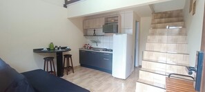 A compact kitchen with a gas stove, a microwave, and a refrigerator. There is a small dining area with stools. - Apto Econômico Mafra  (Mafra)