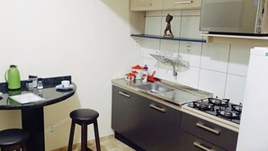 A compact kitchen with a gas stove, a sink, and a small dining area with stools. - Apto Econômico Mafra  (Mafra)