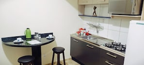 A compact kitchen with a gas stove, a sink, and a small dining area with stools. - Apto Econômico Mafra  (Mafra)