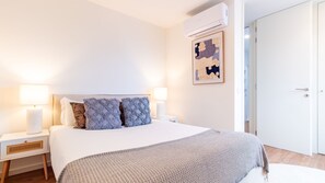 Ein Hotelzimmer mit einem Bett, zwei Nachttischlampen, einer Wand-Klimaanlage und einer Tür.