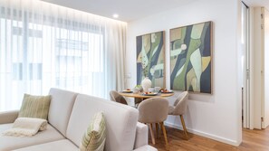 Ein modernes Wohnzimmer mit einer Couch, Sesseln, einem Esstisch mit einer Vase und abstrakten Bildern an der Wand.