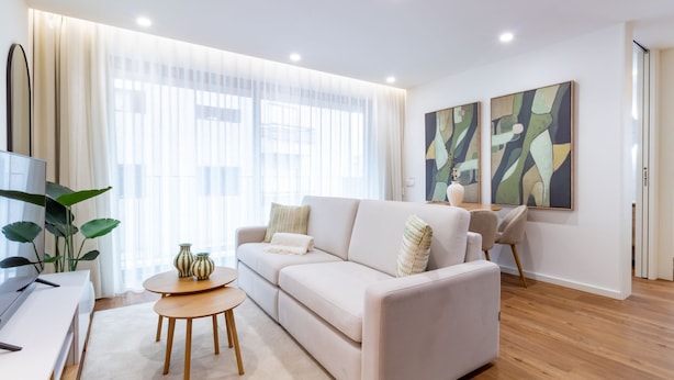 Ein modernes Wohnzimmer mit einer Couch, einem Couchtisch und einem Fernseher auf einem Standfuß.