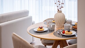 Ein Esstisch mit Pfannkuchen und Beeren, umgeben von weißen Tassen und einer Vase mit Trockenblumen.