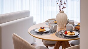 Een eettafel met stapels pannenkoeken en bessen, omringd door witte kopjes en een vaas met gedroogde bloemen.
