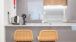 Eine moderne Küche mit einem Kühlschrank von Bosch, einem Wasserkocher, einer Kaffeemaschine und einem Mixer auf der Arbeitsfläche. Vor der Arbeitsfläche stehen zwei Korbstühle.