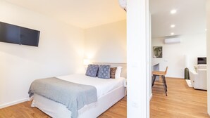 Ein Schlafzimmer mit einem Bett, einem an der Wand montierten Flachbildfernseher und einem Sessel im angrenzenden Raum.