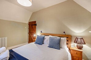 A bedroom with a bed, wooden headboard, bedside table, lamp, and a radiator. - Host & Stay | Lavender Cottage SLEA (Pointon)