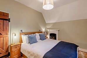 A bedroom with a bed, nightstand, lamp, and a fireplace. - Host & Stay | Lavender Cottage SLEA (Pointon)